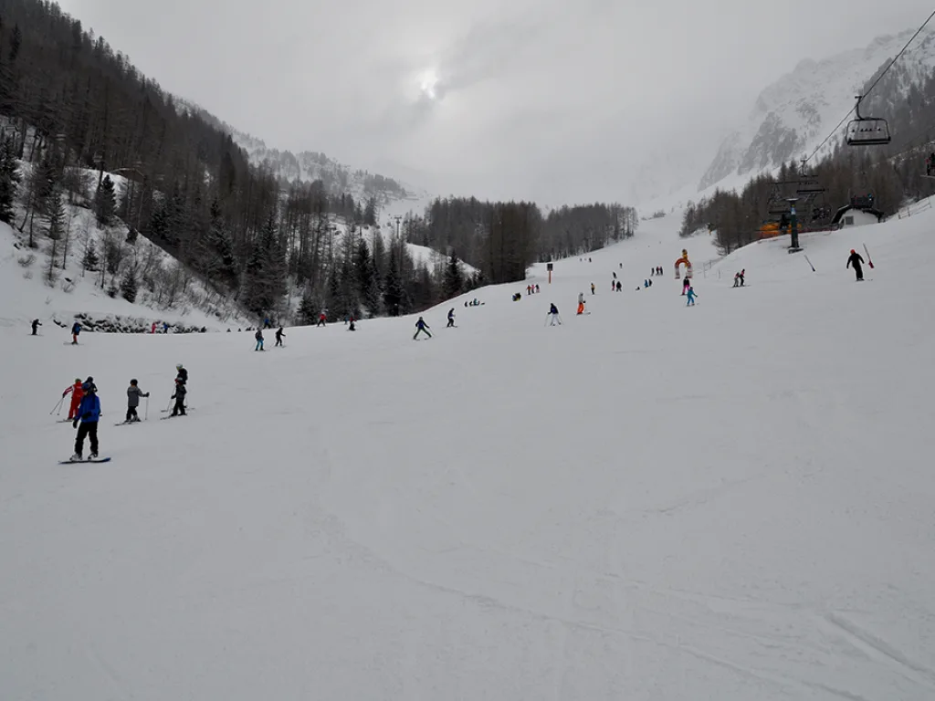 Weite Piste im diesigen Licht, einzelne Fahrende im Tal.